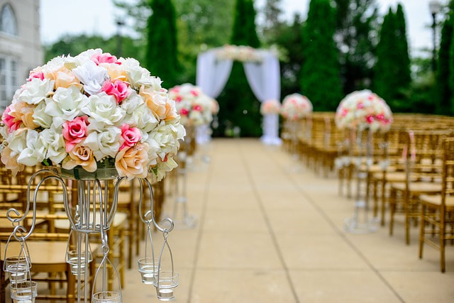 Looking down the aisle from the back at an outdoor wedding before the ceremony begins and guests are seated. Floral bouquets are perched on both sides of the aisle for decoration. 
