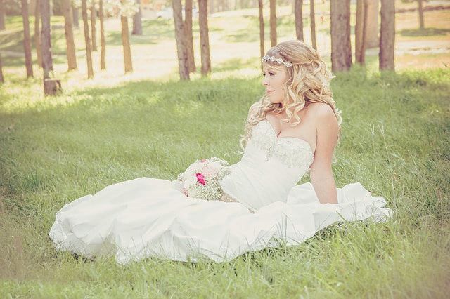 Bride in her white wedding dress sitting in the green grass with trees in the background.