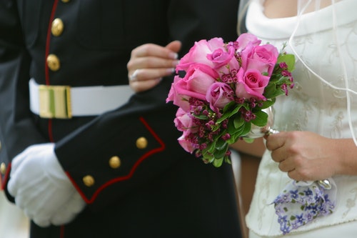 Bride holding pink roses holding on to the arm of her husband wearing a U.S. Marines uniform.